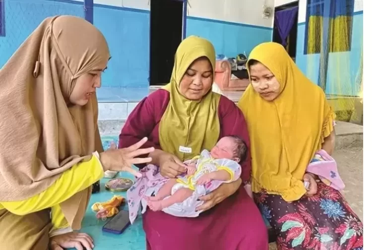 Bidan Desa Sejati Yuliani (kiri) menghibur Amira Hilyatun Nisak yang digendong dukun bayi Halisa di samping Subaidah (kanan) Selasa (30/1). (ANIS BILLAH/JPRM)