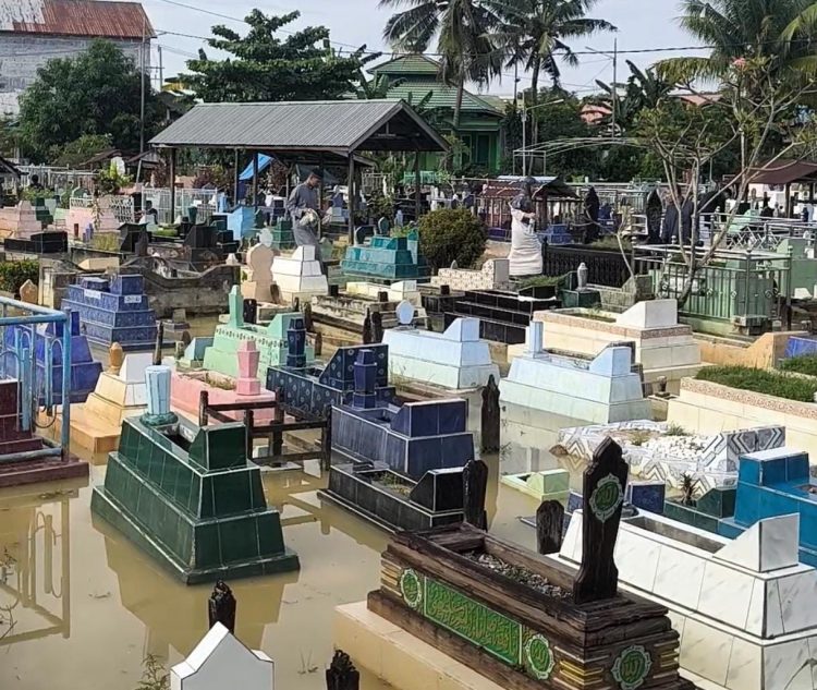 Banjir rob rendam TPU Bontang Kuala saat Idulfitri. Warga tetap ziarah meski harus berjalan di tengah genangan air laut.